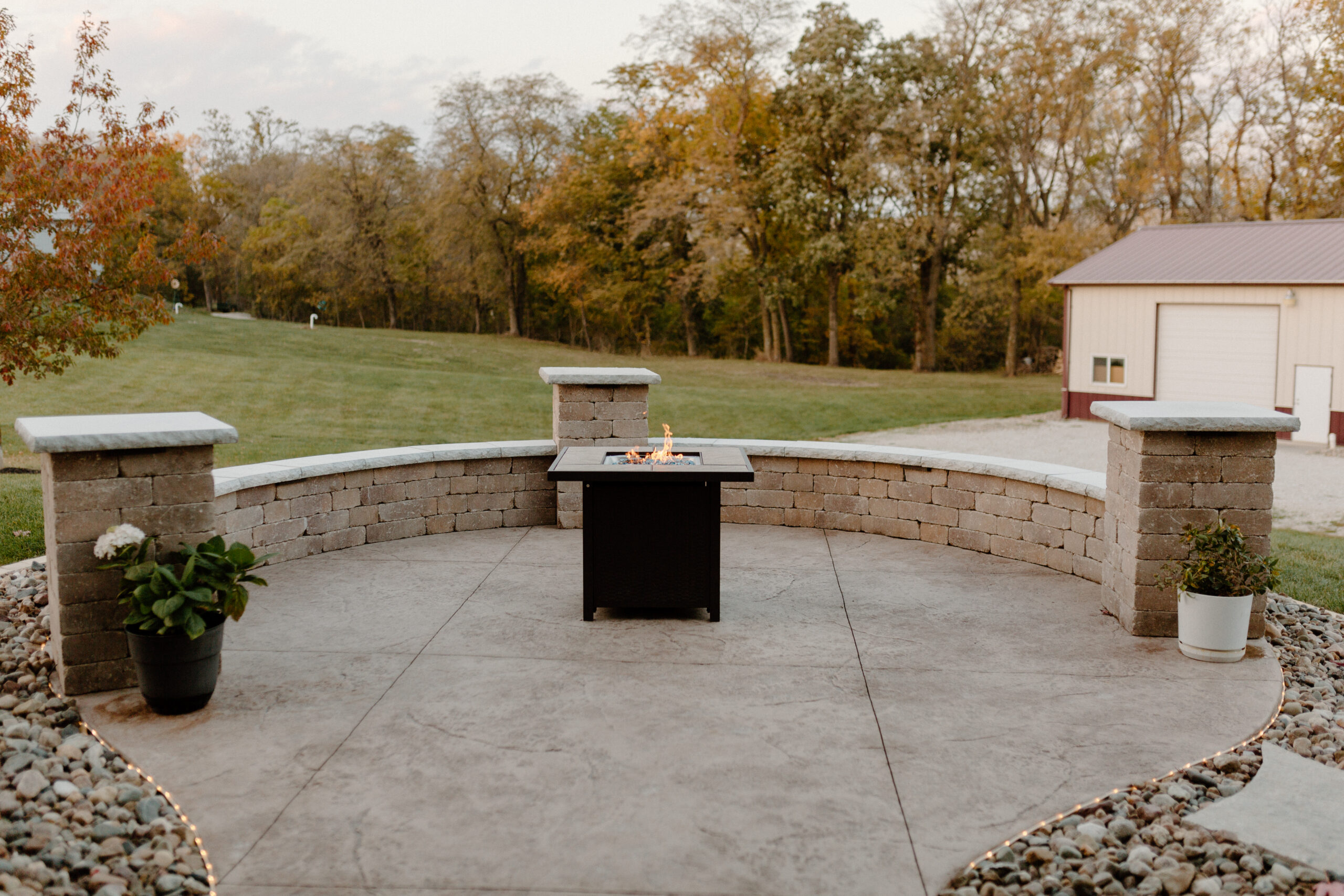 Fire pit with a seating wall made from concrete, brick and stone with a rock surround. Des Moines, Iowa Landscapes