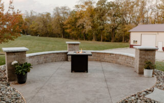 Fire going in a fire pit with a surrounding seating wall on a concrete patio - Des Moines Landscape