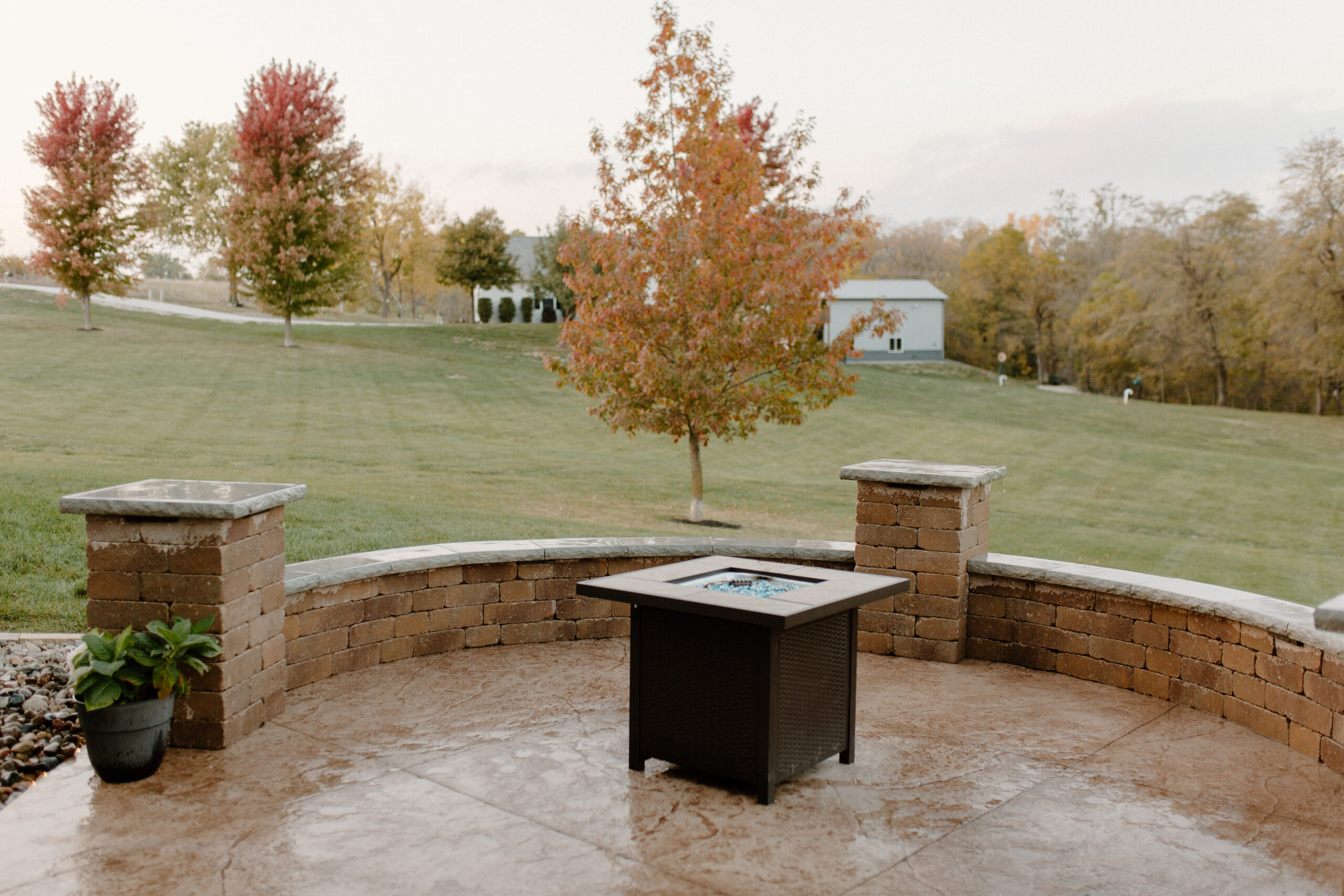 Fire pit on a patio surrounded by a stone seating semicircle with new trees planted in the background - Des Moines, Iowa Landscape Design