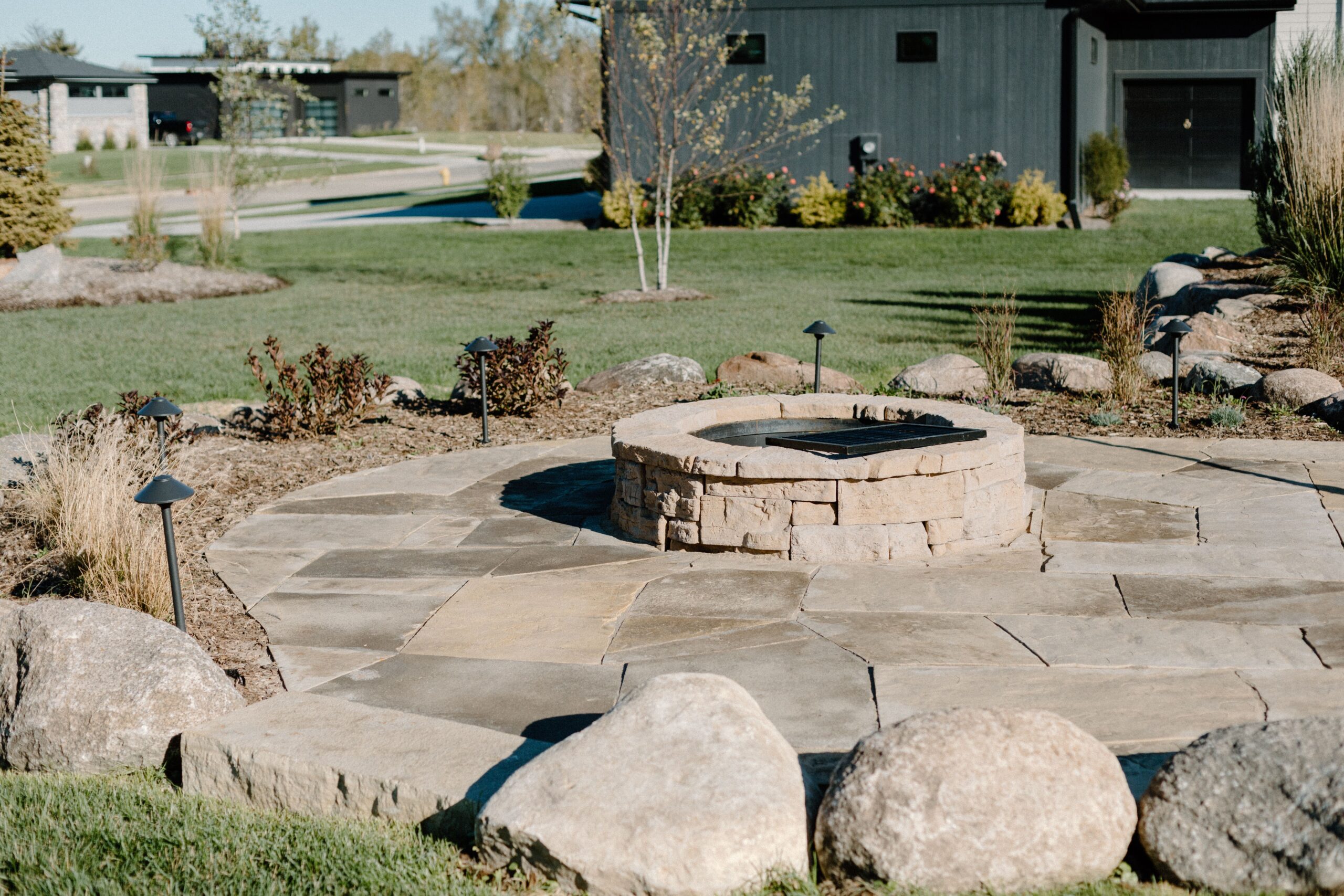 Fire pit installation on a stone patio. with lighting feature and newly planted trees - Iowa Landscape Design by Creative Nature